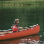 woman in red vest riding red kayak on lake during daytime