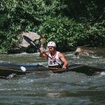 A man skillfully navigating a kayak through river rapids amid lush greenery.