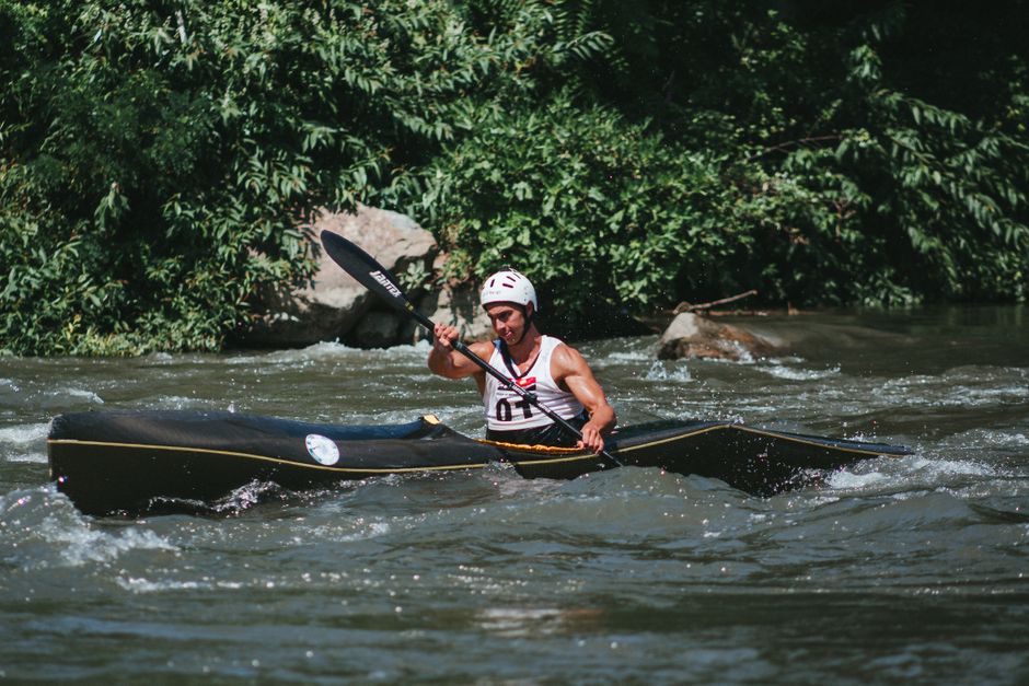 A man skillfully navigating a kayak through river rapids amid lush greenery.